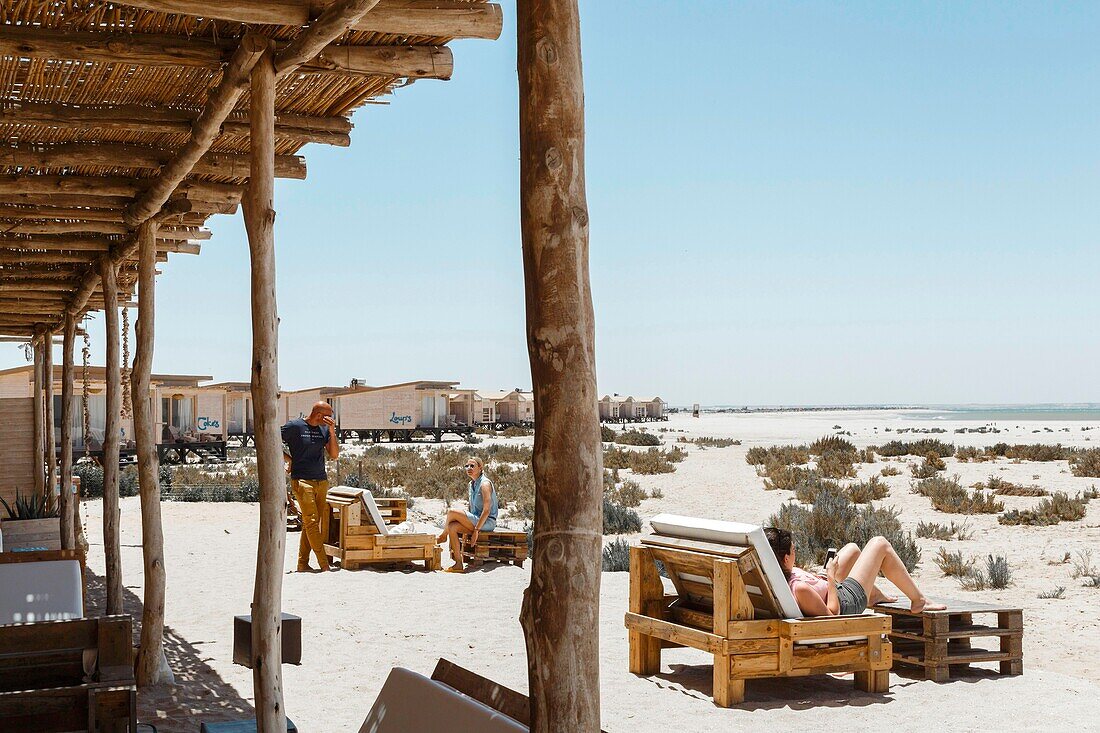 Marokko, Oued Ed-Dahab, Dakhla, Ocean Vagabond Lassarga Eco-lodge, Personen in einer Öko-Lodge am Strand in einer Wüstenlandschaft