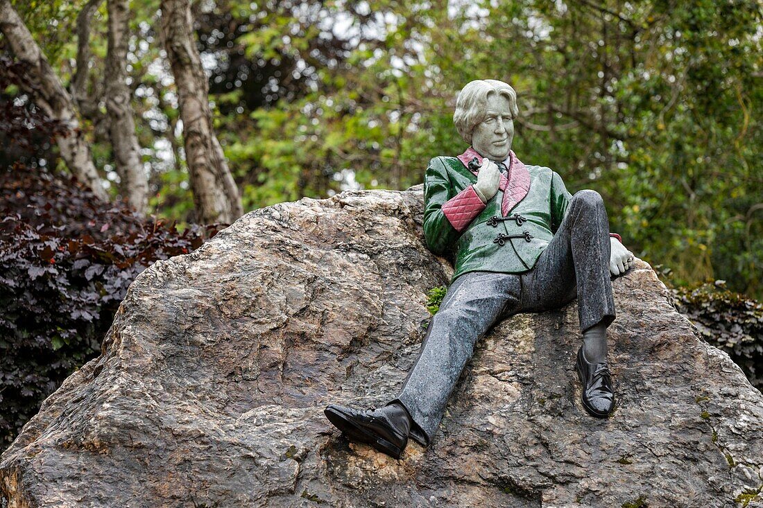 Ireland, Dublin, Merrion Square, memorial tribute to Irish author Oscar Wilde known for his dissolute life, set of statues nude woman and writer nonchalantly lying on a rock in full green and red suit jacket