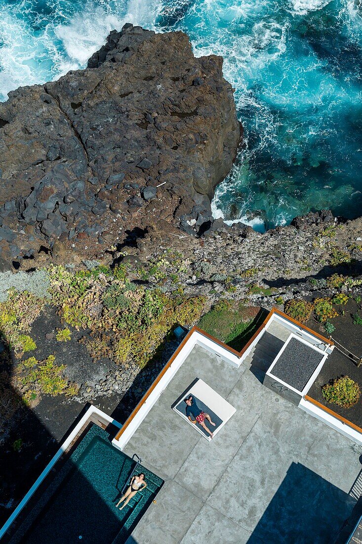 Spanien, Kanarische Inseln, La Palma, Touristen ruhen sich am Rande eines Swimmingpools am Meer aus (Luftaufnahme)