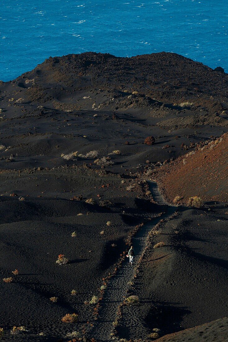 Spanien, Kanarische Inseln, La Palma, Wanderer auf einem Wanderweg in einer wüstenhaften und vulkanischen Umgebung bei Sonnenaufgang