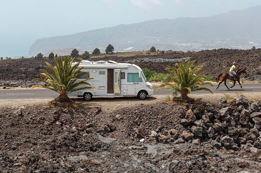 Spain, Canary Islands, La Palma, motorhome and rider riding on a road in a volcanic environment