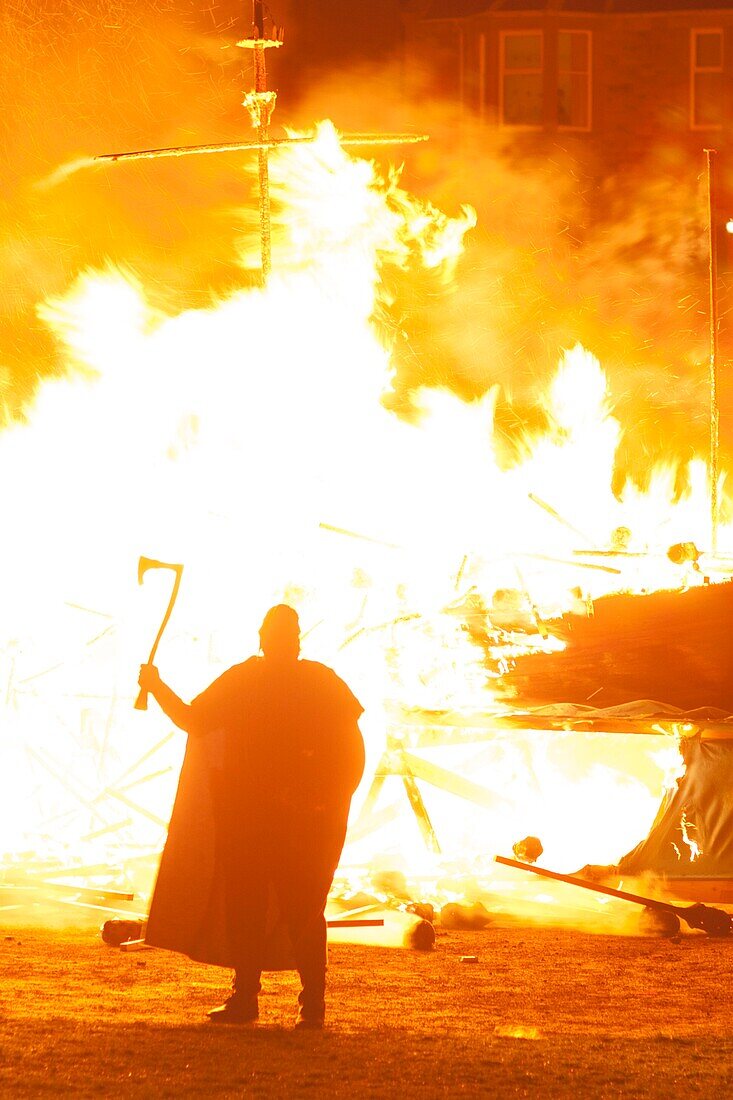 Vereinigtes Königreich, Schottland, Shetlandinseln, Festland, Lerwick, Up Helly Aa Fest, Guizer schwingt eine Axt vor dem brennenden Langschiff