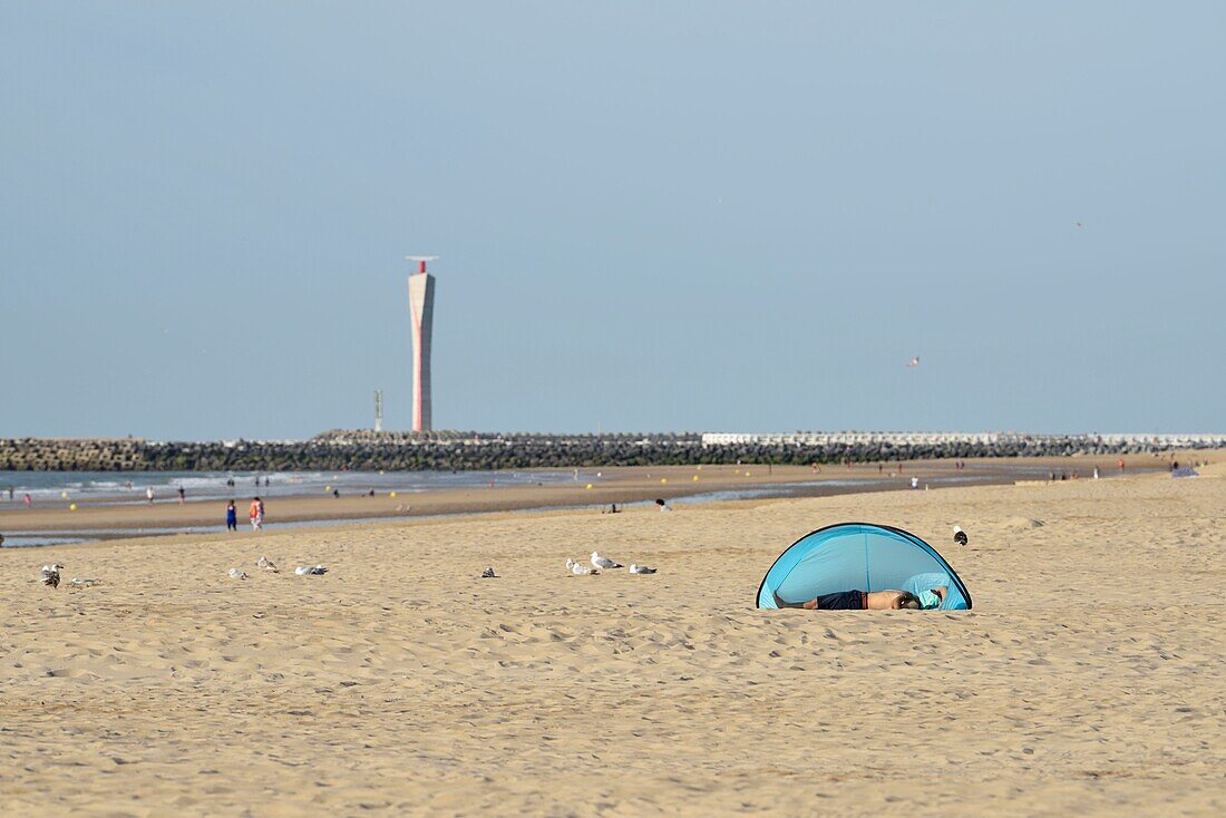 Belgien, Westflandern, Ostende, Strand und Leuchtturm, Mann liegt unter einem blauen Zelt