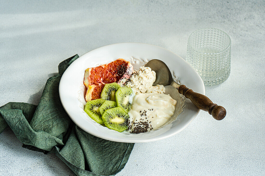 A well-balanced breakfast setting featuring a white bowl with cottage cheese, natural yogurt, and chia seeds, accompanied by kiwi and Sicilian orange slices