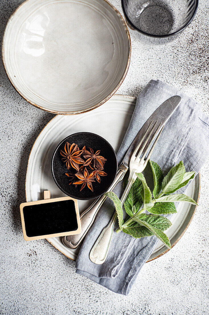 A beautifully arranged summer table setting featuring a mint theme with fresh mint leaves, stylish star anise in a small ceramic bowl, and elegant gray-toned dinnerware on a textured surface