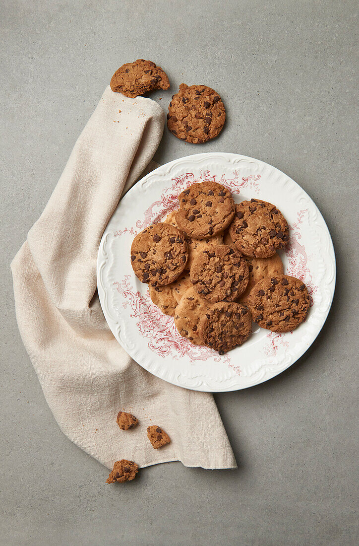 Chocolate chip cookies spread on a vintage ornate plate, accented by a beige linen napkin, offer a timeless and elegant teatime appeal