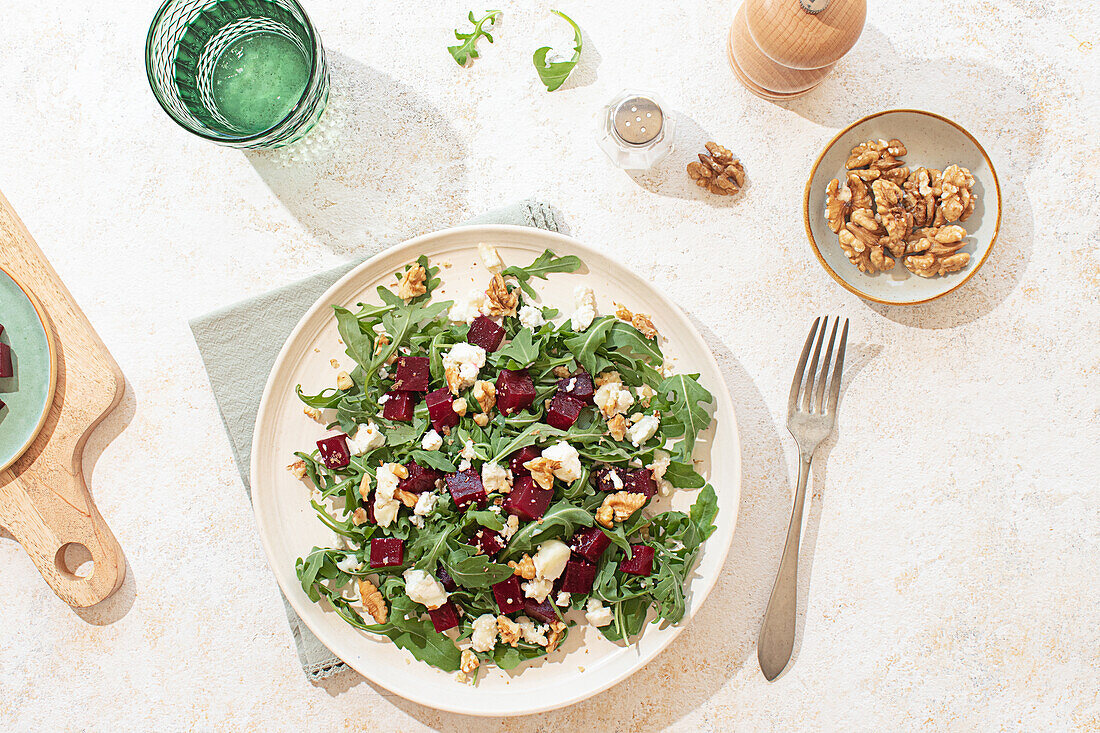 A beautifully styled arugula salad with goat cheese, walnuts, and beetroot on a light beige plate. Natural light highlights the vibrant colors and textures, creating a fresh and inviting atmosphere