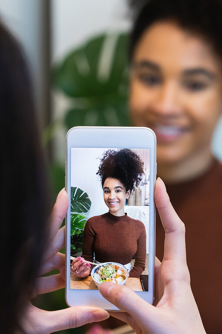 Unrecognizable female taking photo of black friend eating tasty poke dish in restaurant