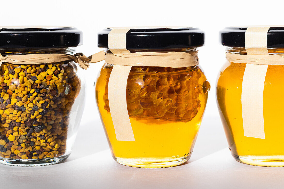 Glass jars with fresh honey and bee pollen placed in row on table