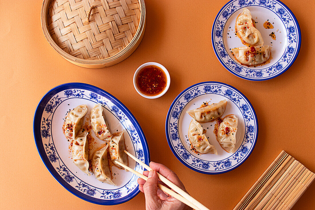 A vibrant image showcasing steamed Chinese dumplings, drizzled with spicy sauce and sesame seeds, elegantly plated on blue and white porcelain dishes against a warm orange background