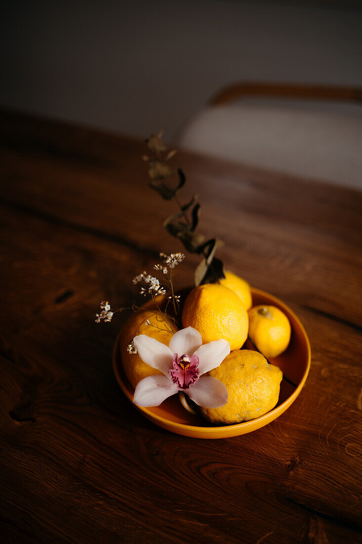 Ein geschmackvolles Arrangement aus reifen Zitronen und einer zarten Orchidee in einer Keramikschale auf einer Holzfläche