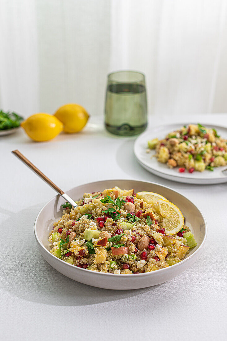 A vibrant quinoa salad mixed with curry spices, fresh vegetables, nuts, and lemon slices, presented in a bowl on a white table, with soft backlighting.