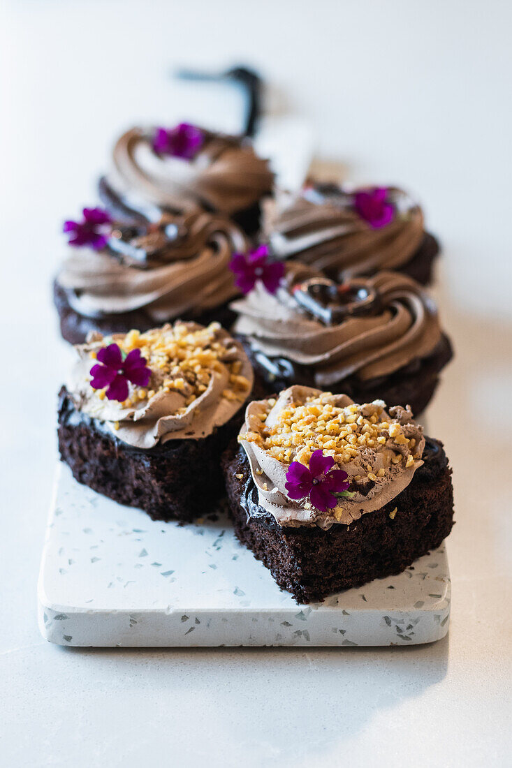 High angle of vegan chocolate sponge cakes with whipped cream and flower decorations served on cutting board on table in bakery