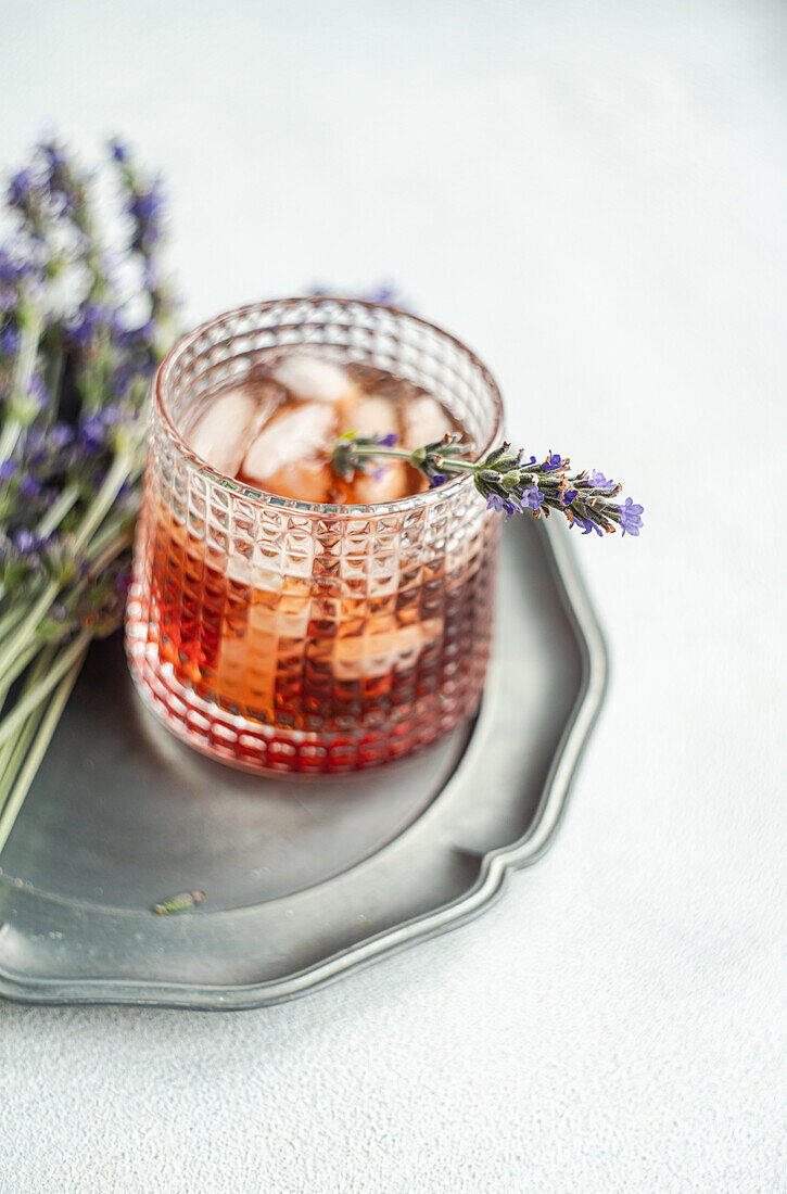 An elegant cognac cocktail adorned with a sprig of fresh lavender, presented in a textured glass on a metal tray, setting a sophisticated and aromatic scene