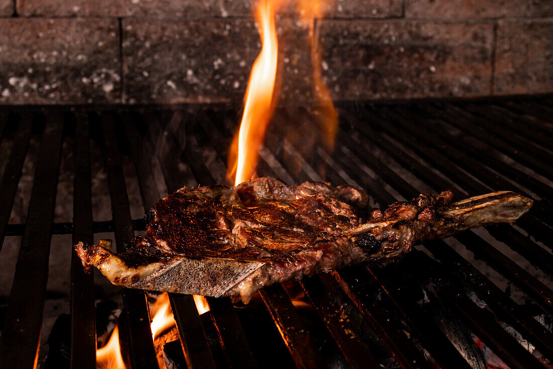 A juicy steak with a golden-brown crust cooks on a grill, with vibrant flames licking the edges in a rustic outdoor setting, capturing the essence of traditional Mexican home cooking.