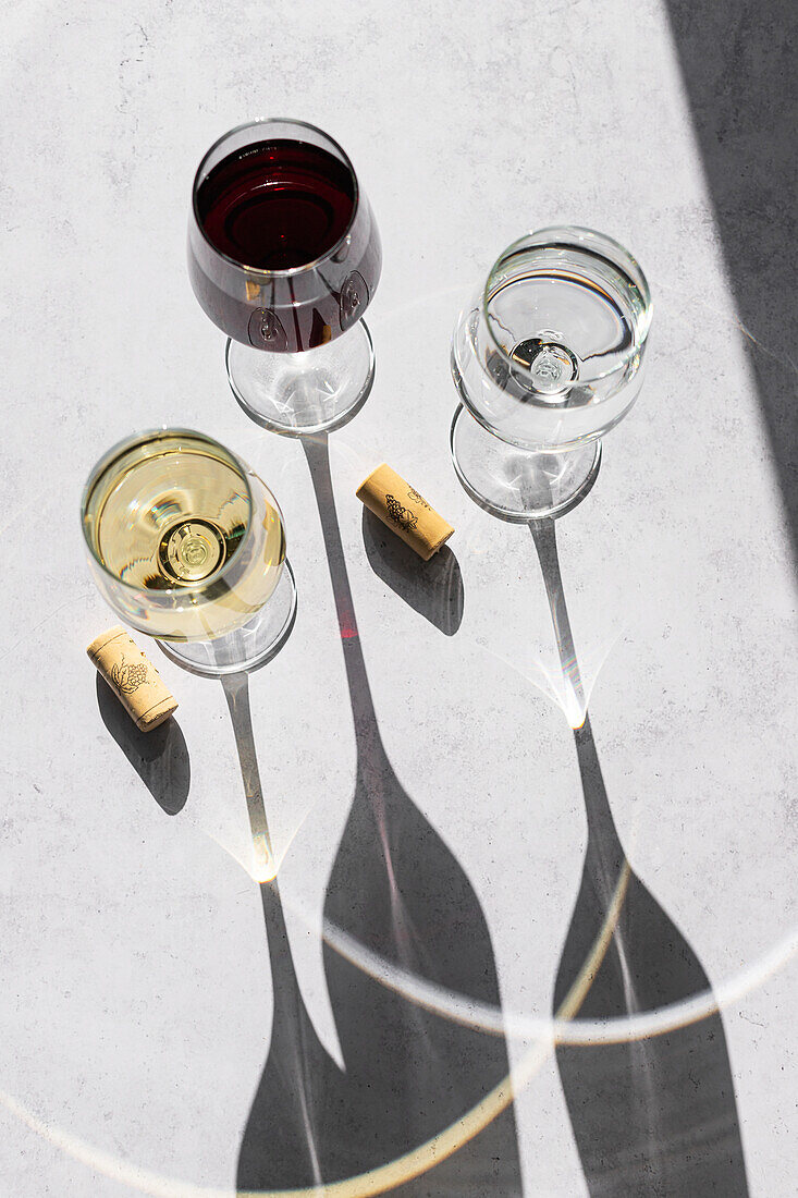 Three wine glasses filled with red, white, and no wine cast long shadows on a textured surface, showcasing a minimalistic and elegant design.