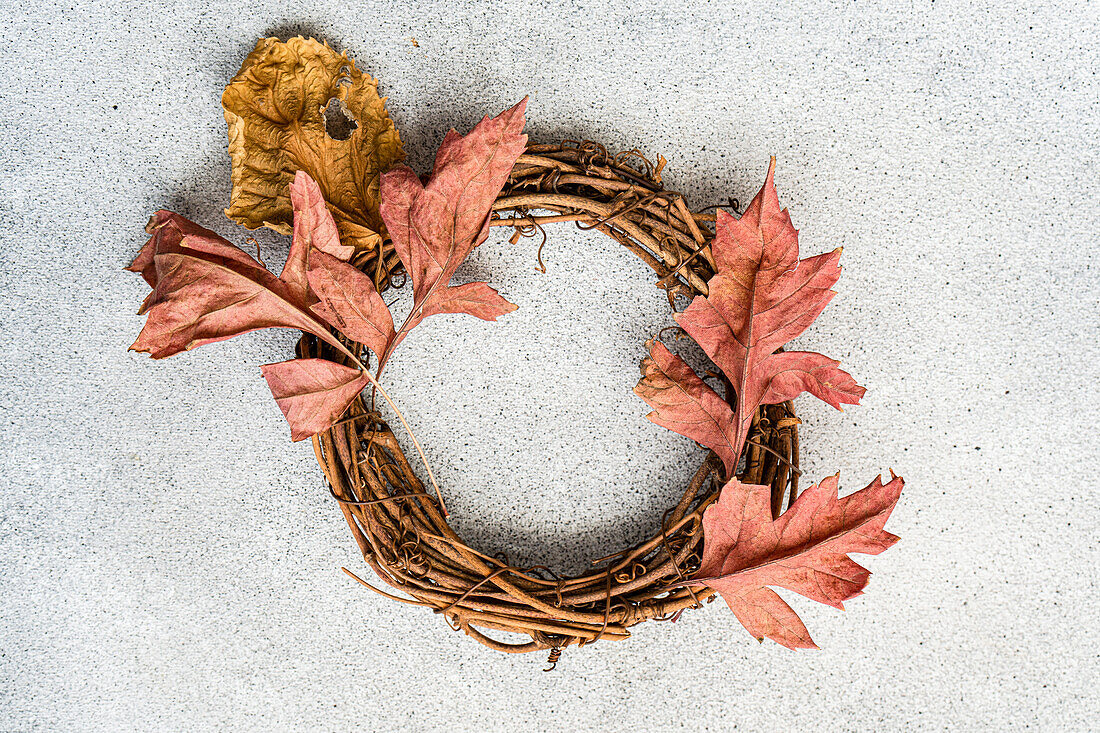 Ein farbenfroher, herbstlicher Kranz aus gedrehten Zweigen und orangefarbenen Blättern vor einem strukturierten grauen Hintergrund