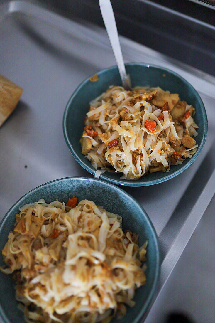 From above two teal bowls filled with homemade stir-fried noodles, featuring sliced vegetables and tofu, are situated on a grey kitchen counter, showcasing a simple, healthy meal prepared at home