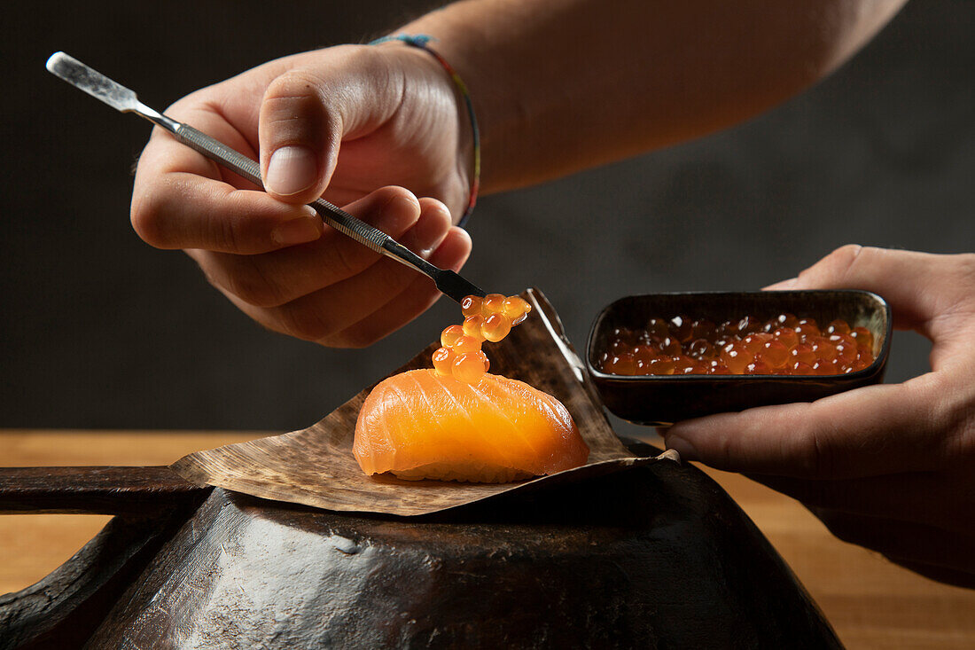 A skilled chef carefully garnishes a piece of salmon sushi with caviar, using precise tools and techniques to ensure perfect presentation and flavor