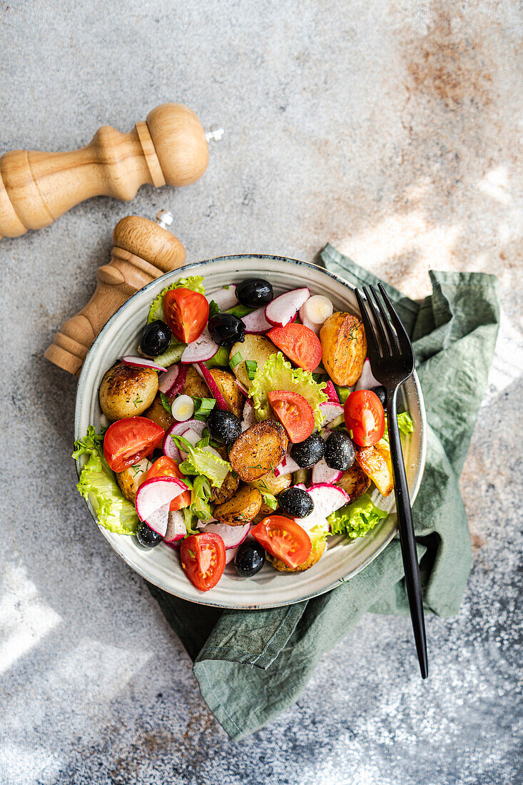 Top view of a rustic Mediterranean potato salad with spring potatoes, black olives, cherry tomatoes, spring onions, crisp lettuce, and radishes, served with a touch of elegance