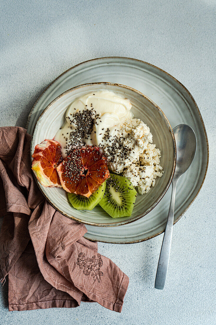 Top view of nutritious breakfast bowl featuring creamy cottage cheese, natural yogurt, chia seeds, fresh kiwi slices, and a juicy wedge of Sicilian orange