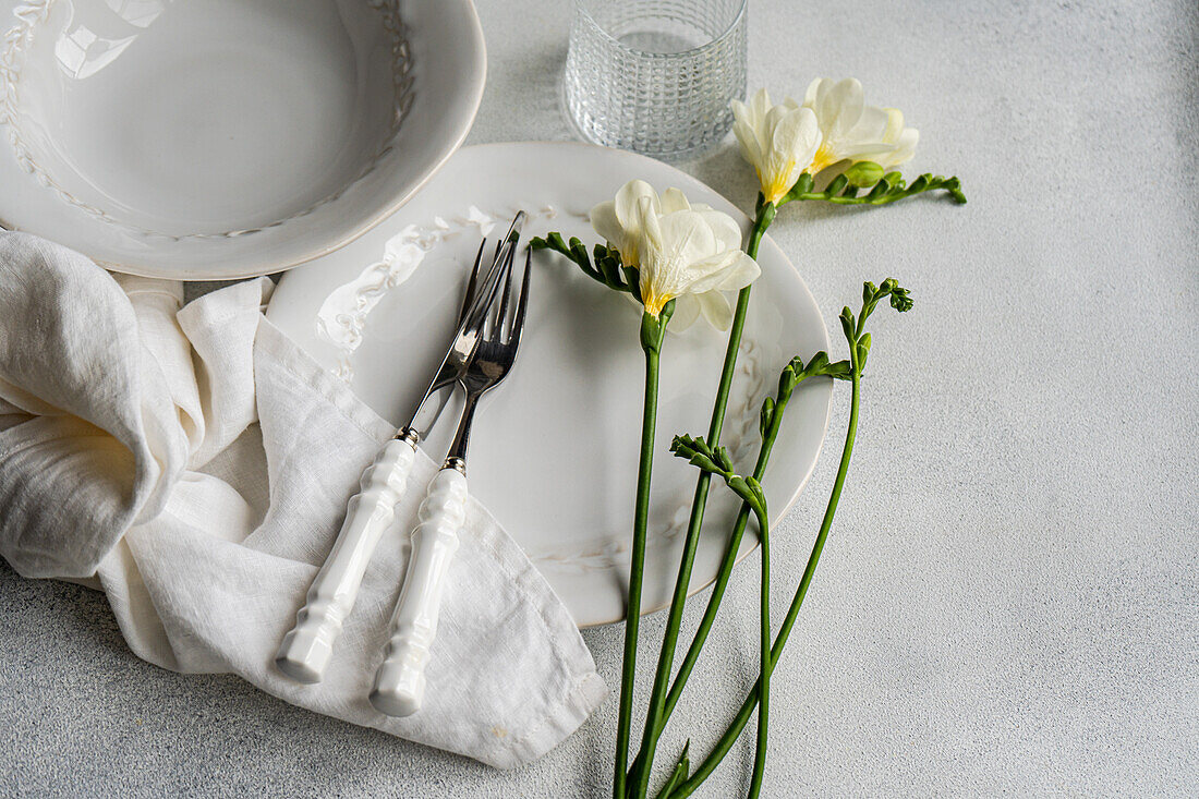 A sophisticated table setting theme featuring delicate white Freesia flowers, elegant plates, and silver cutlery with white handles, complemented by a soft linen napkin