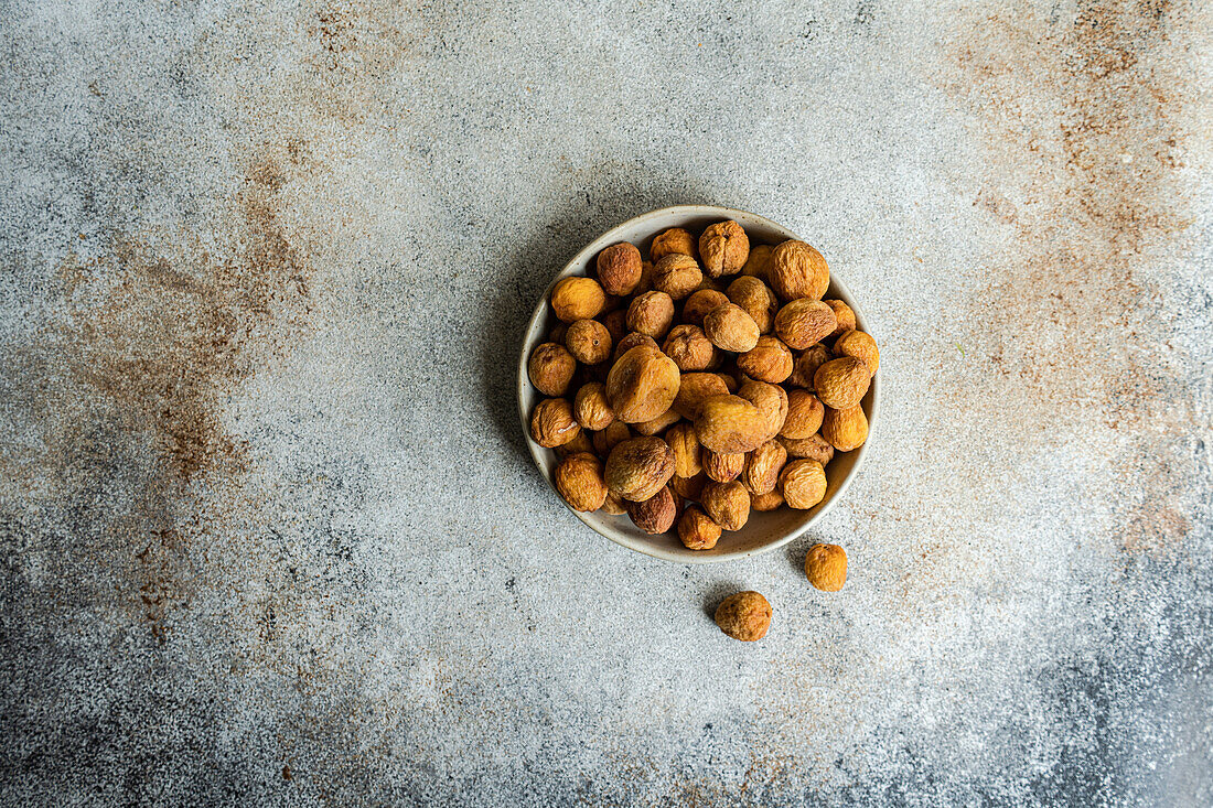 Bowl of sun-dried wild apricots, known as Arashan Kandak, on a textured surface, a healthy snack from Central Asia