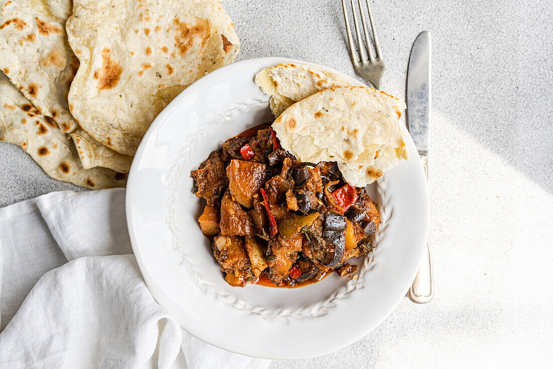 Ein köstlicher Gemüseeintopf aus Auberginen, Tomaten, Kartoffeln, Paprika, Zwiebeln und Knoblauch, garniert mit frischem Basilikum, serviert mit warmem hausgemachtem Fladenbrot