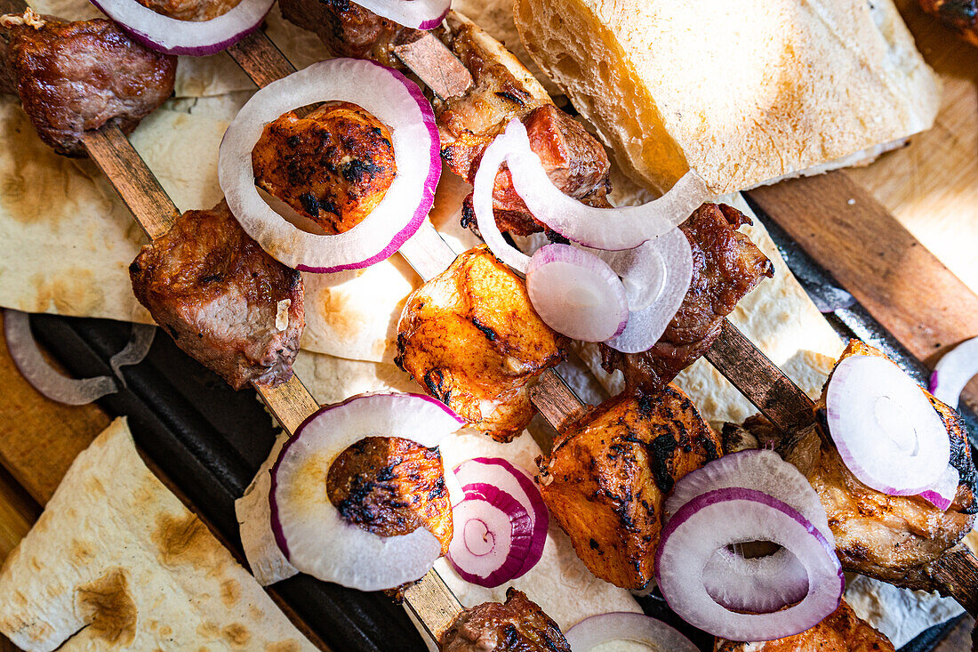 Nahaufnahme von saftigen georgischen mtsvadi, aufgespießtem und gegrilltem Fleisch, begleitet von geschnittenen roten Zwiebeln und frischem Brot, das die reichen kulinarischen Traditionen Georgiens zeigt