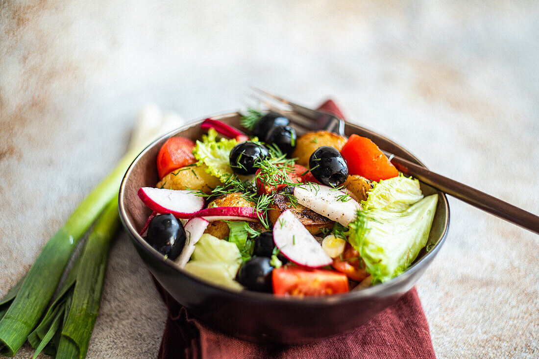 A beautifully arranged Mediterranean salad in a bowl, showcasing roasted potatoes, black olives, cherry tomatoes, crisp radishes, and lettuce, accented with fresh dill