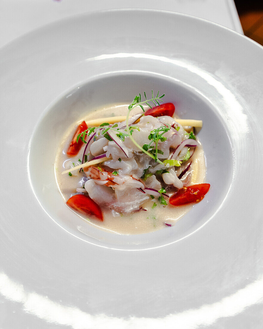 Ein lebhaftes Krabben-Ceviche, garniert mit Kirschtomaten, Limetten und frischen Kräutern, serviert in einer weißen Schale.