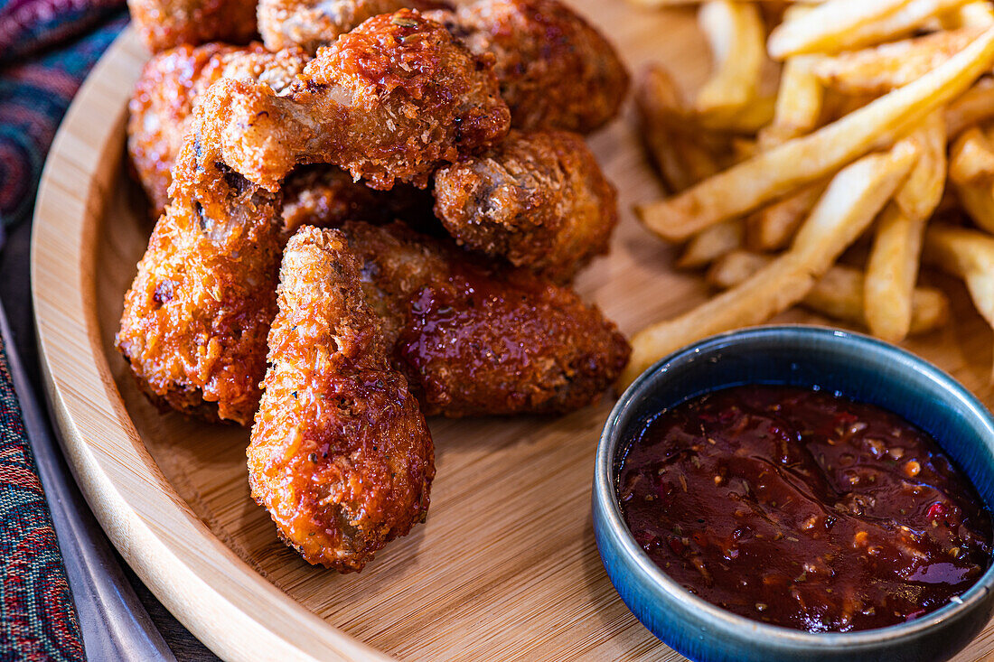 Knusprig gebratene Hähnchenhüften, serviert auf einem Holzteller zusammen mit goldenen Pommes frites und einer Schale mit reichhaltiger BBQ-Sauce, perfekt für eine herzhafte Mahlzeit.