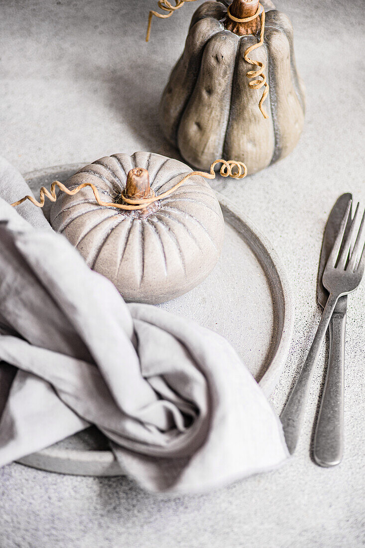 A stylish autumnal table arrangement featuring unique ceramic pumpkins, a draped linen napkin, and modern cutlery on a textured surface