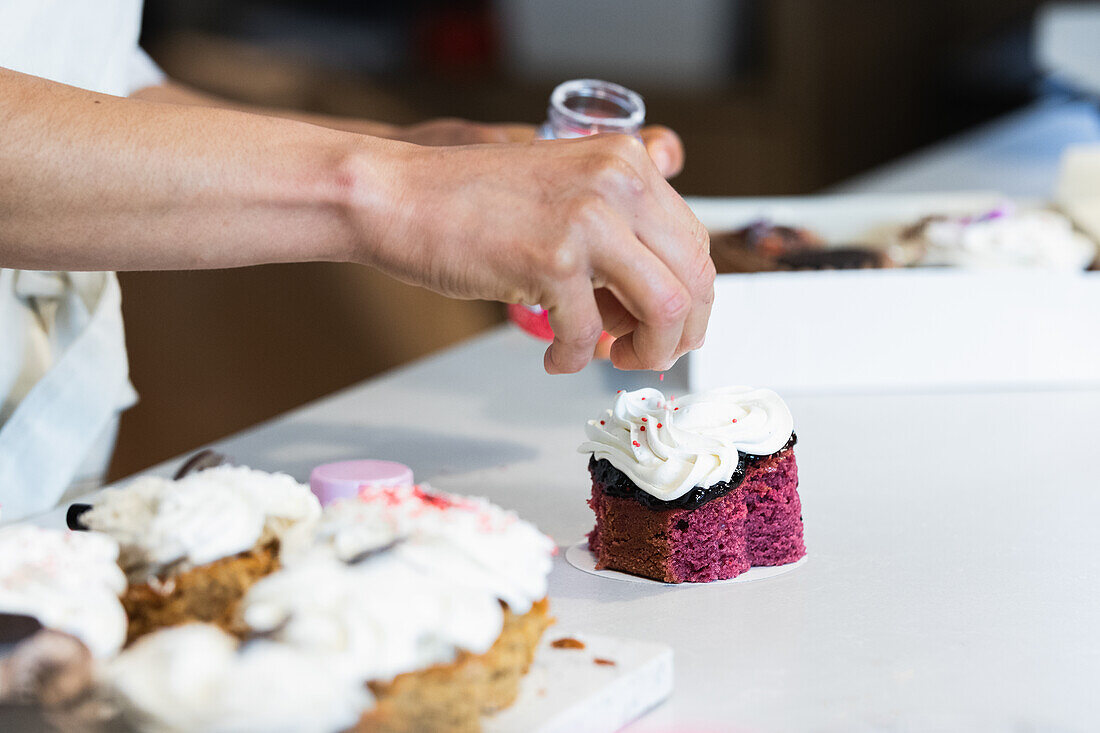 Crop anonymous cook sprinkling vegan velvet cake while preparing desserts in bakery