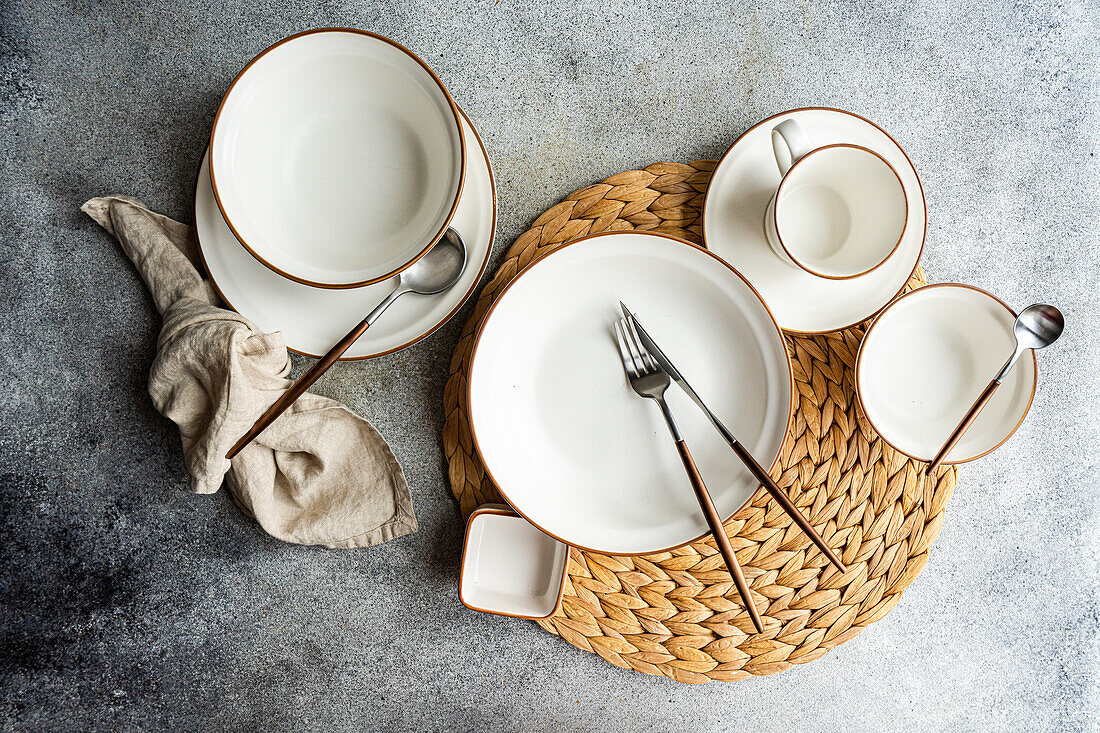 Top view of a stylish table setting featuring bright ceramic dinnerware and sleek cutlery on a woven placemat, ready for a refined dining experience.