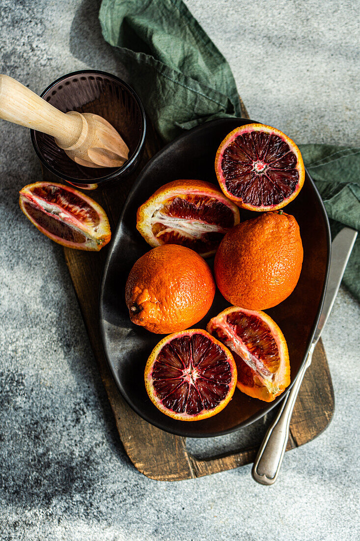 A vibrant arrangement of sliced blood oranges next to a manual juicer on a dark serving tray, with a fabric napkin adding texture