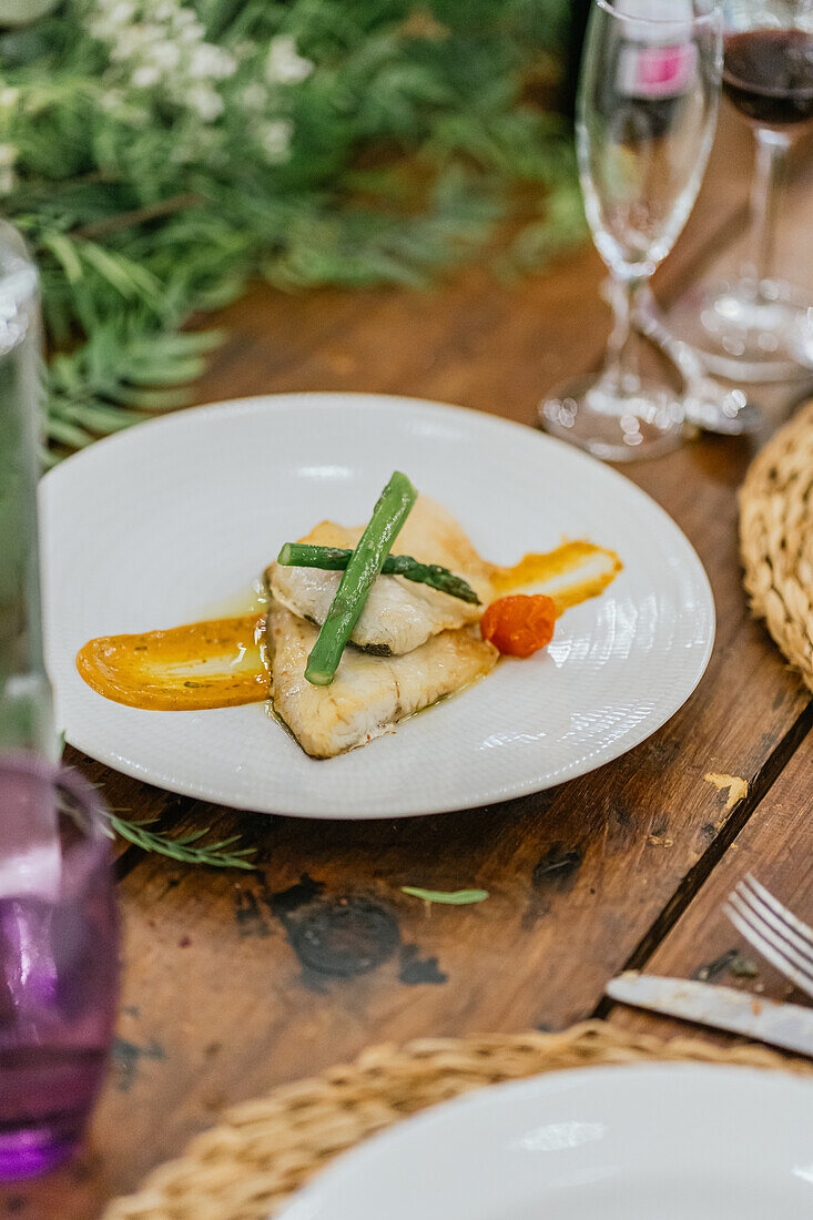 A delicately cooked fish fillet served with fresh asparagus and a smooth puree, plated on white china against a rustic wooden table backdrop