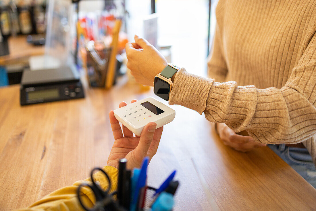 Customer using a smartwatch to perform a contactless payment at a store's digital point-of-sale terminal.