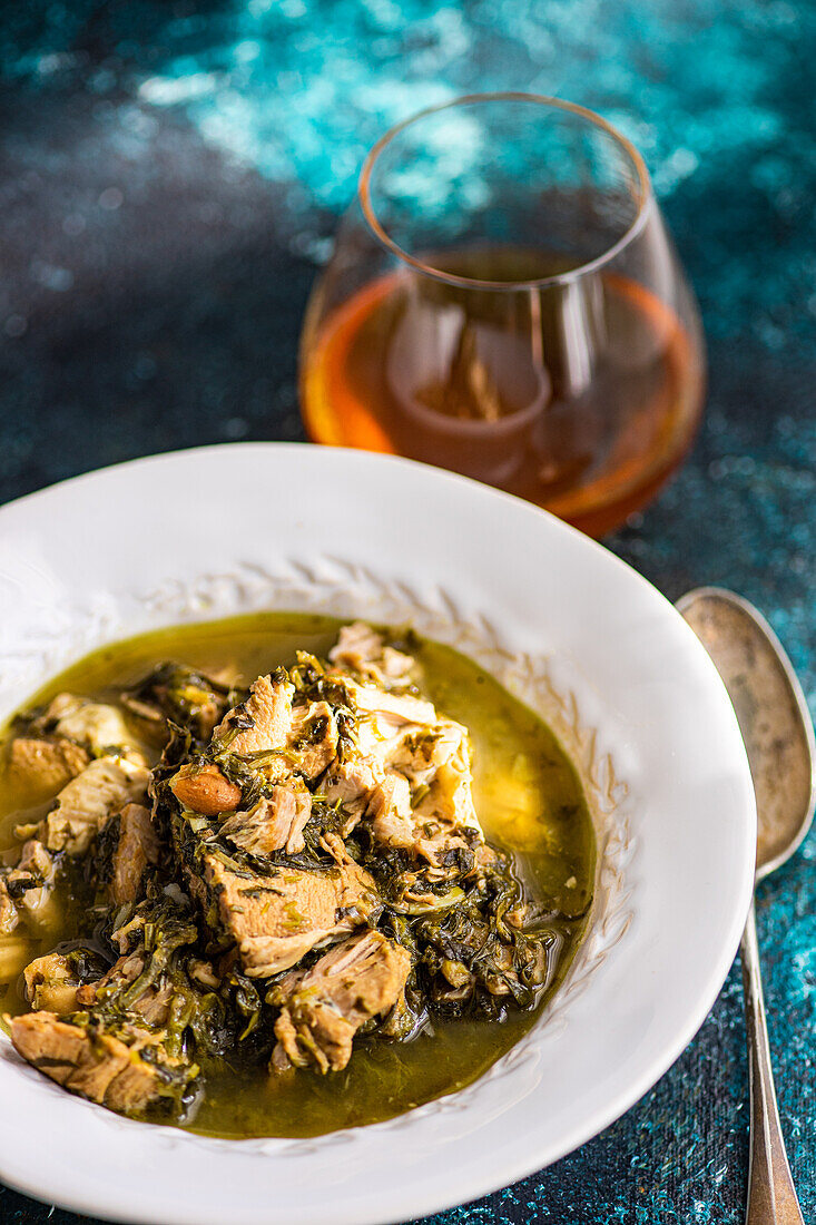 Delicious Georgian spring dish featuring stewed meat cooked with white wine, green plums, and assorted fresh herbs including tarragon, coriander, parsley, and green onions, served in a white bowl.