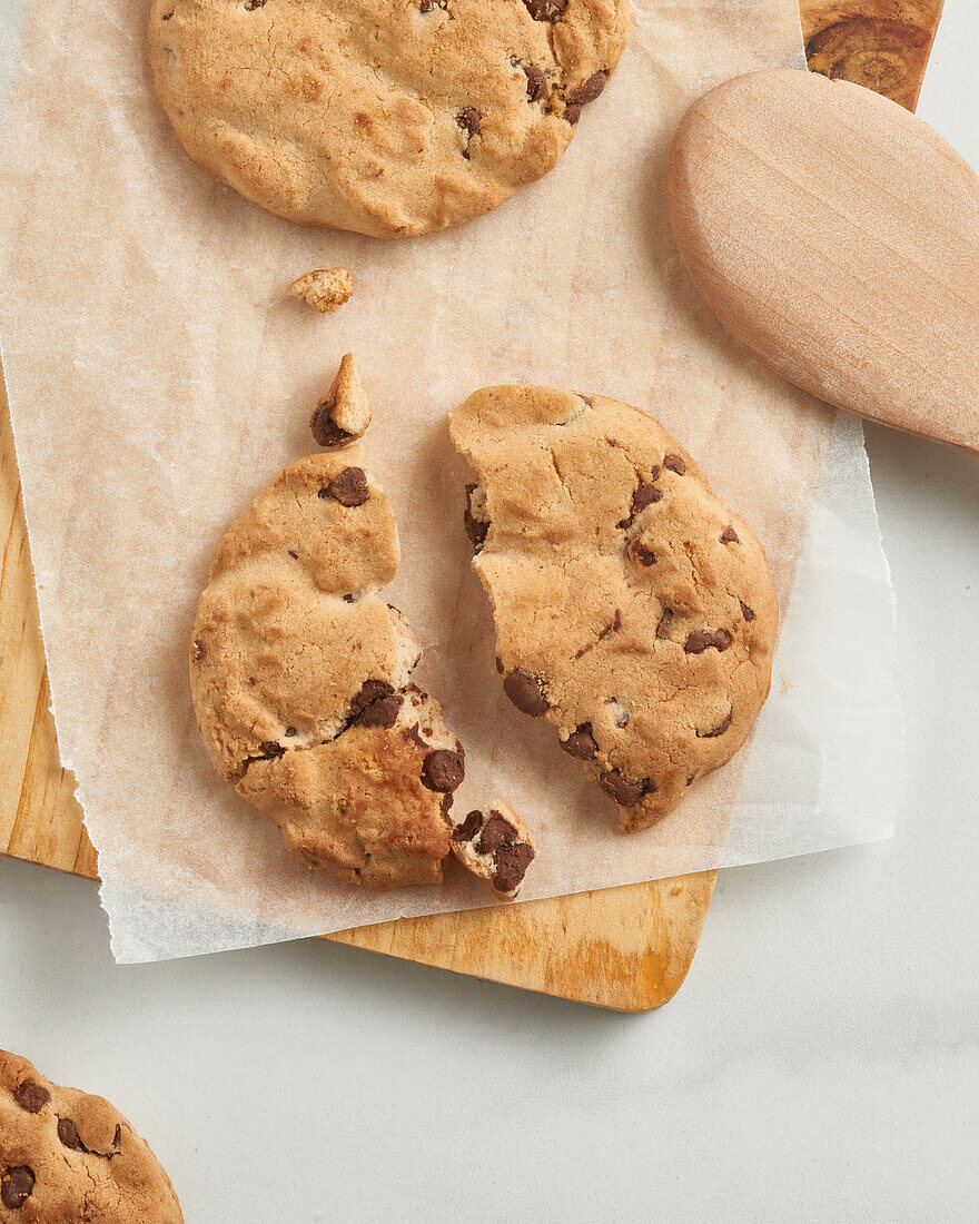 A delicious top view of chocolate chip cookies on parchment paper, partially resting on a wooden board