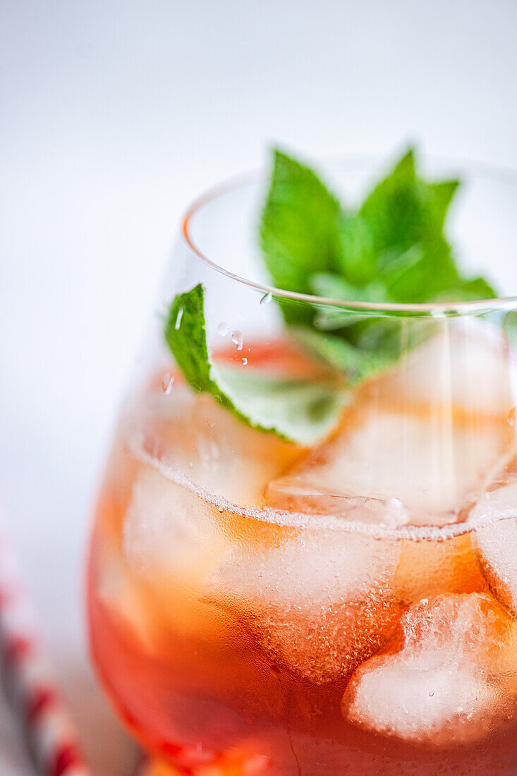 A close-up view of a refreshing Coke cocktail, beautifully garnished with fresh, vibrant mint leaves. The beverage is served in a clear glass filled with ice cubes, capturing the essence of a perfect summer drink.