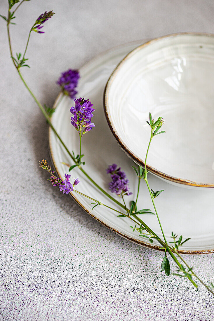 Minimalistisch gedeckter Sommertisch mit einem alten Teller und wilden Alfalfa-Blumen, die einen Hauch von natürlicher Eleganz vermitteln.