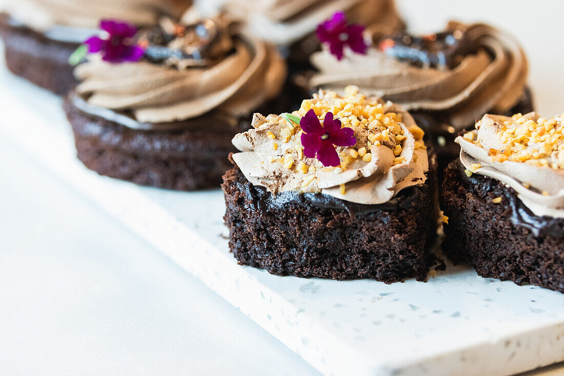 High angle of vegan chocolate sponge cakes with whipped cream and flower decorations served on cutting board on table in bakery