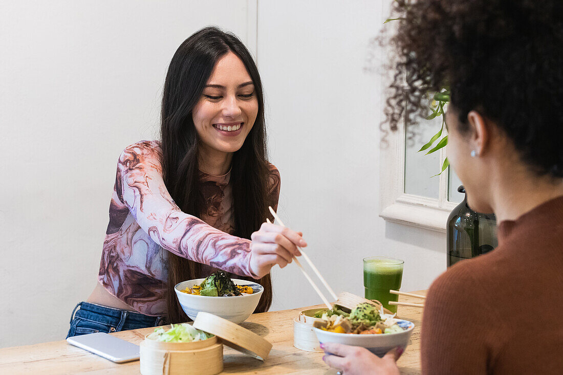 Diverse female friends sitting at table and eating tasty poke while spending weekend in restaurant