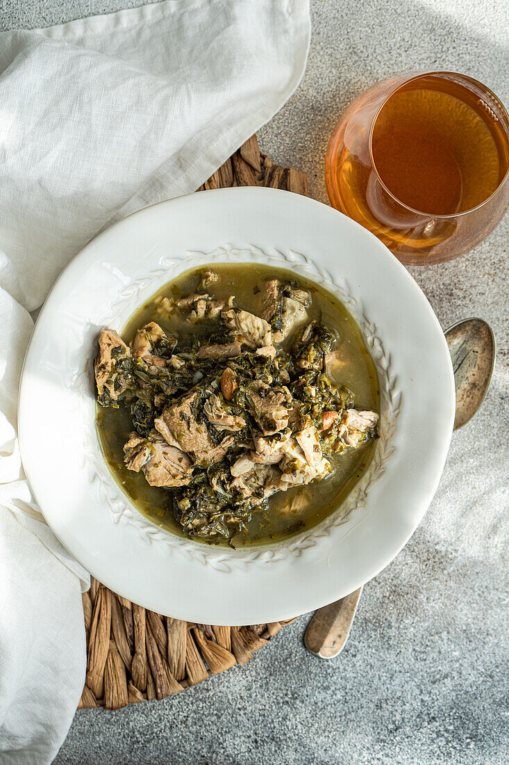 Top view of traditional Georgian dish of stewed meat cooked with white wine, tangy green plums, and a mix of fresh herbs including tarragon, coriander, parsley, and green onions, served in a white bowl.