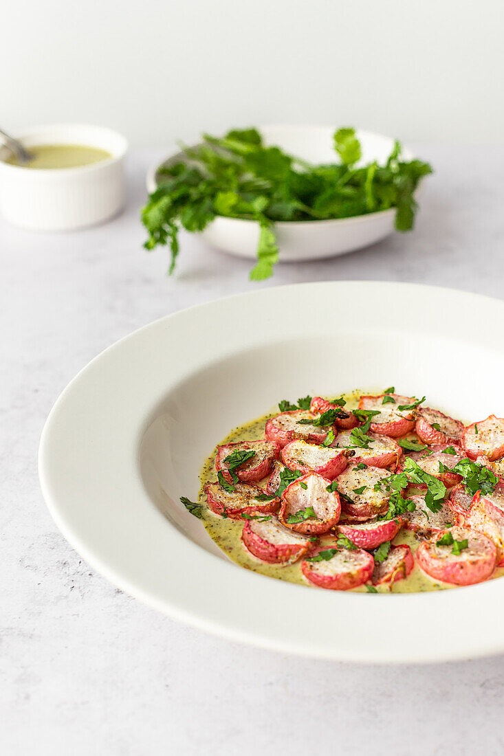 A dish of roasted radishes drizzled with a vibrant green tahini sauce, garnished with fresh parsley, shot from a high angle.