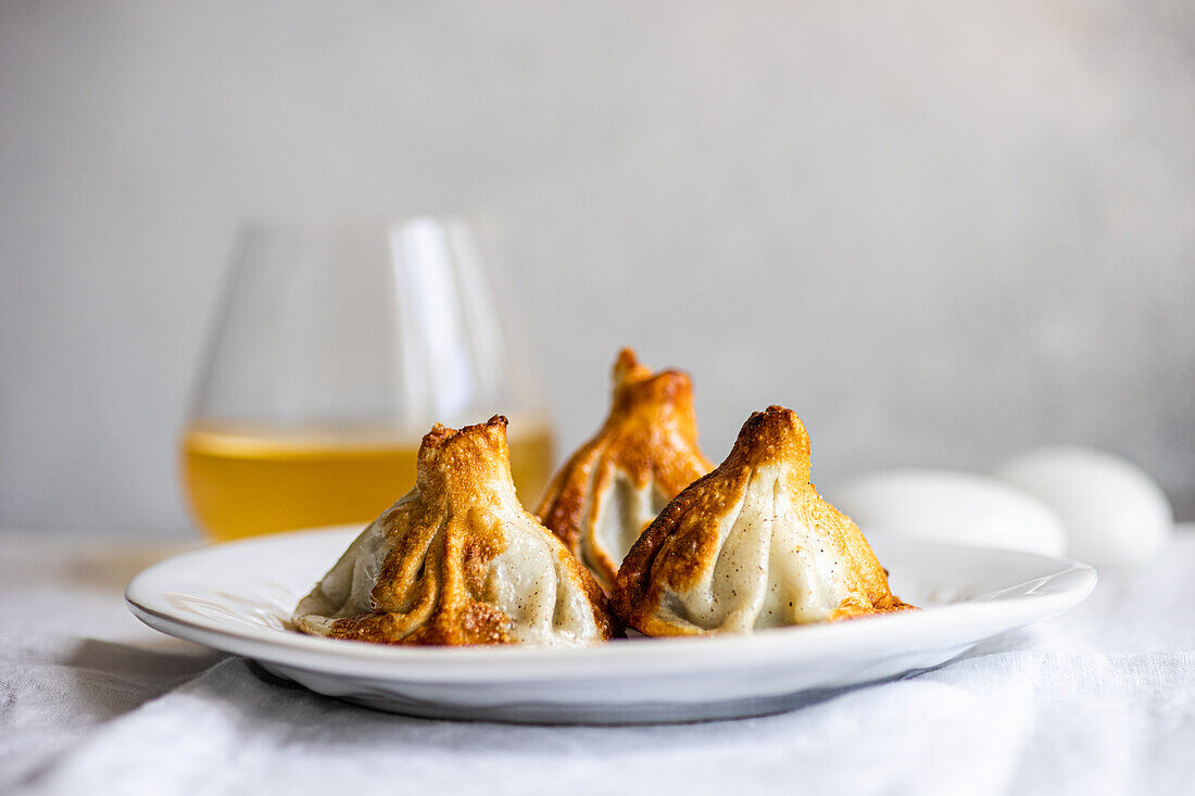 Authentic Georgian khinkali dumplings served on a white plate, expertly cooked A clear glass of white wine complements the scene, heightening the culinary appeal