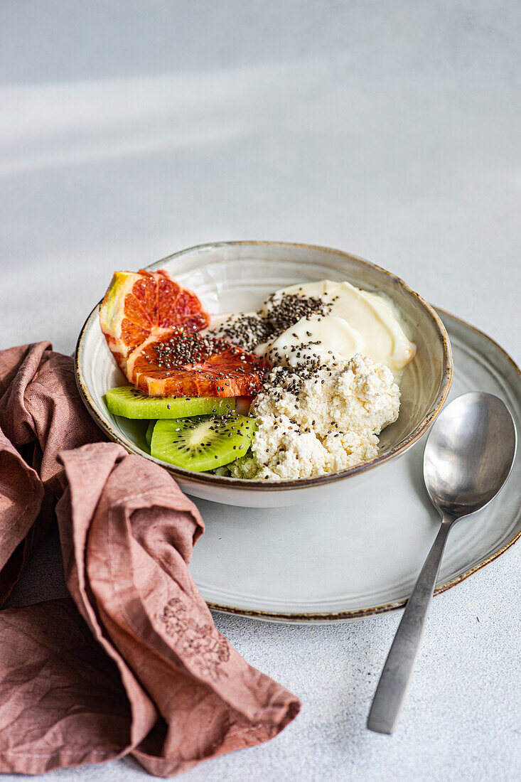 A nutritious breakfast bowl featuring creamy cottage cheese, natural yogurt, chia seeds, fresh kiwi slices, and a juicy wedge of Sicilian orange