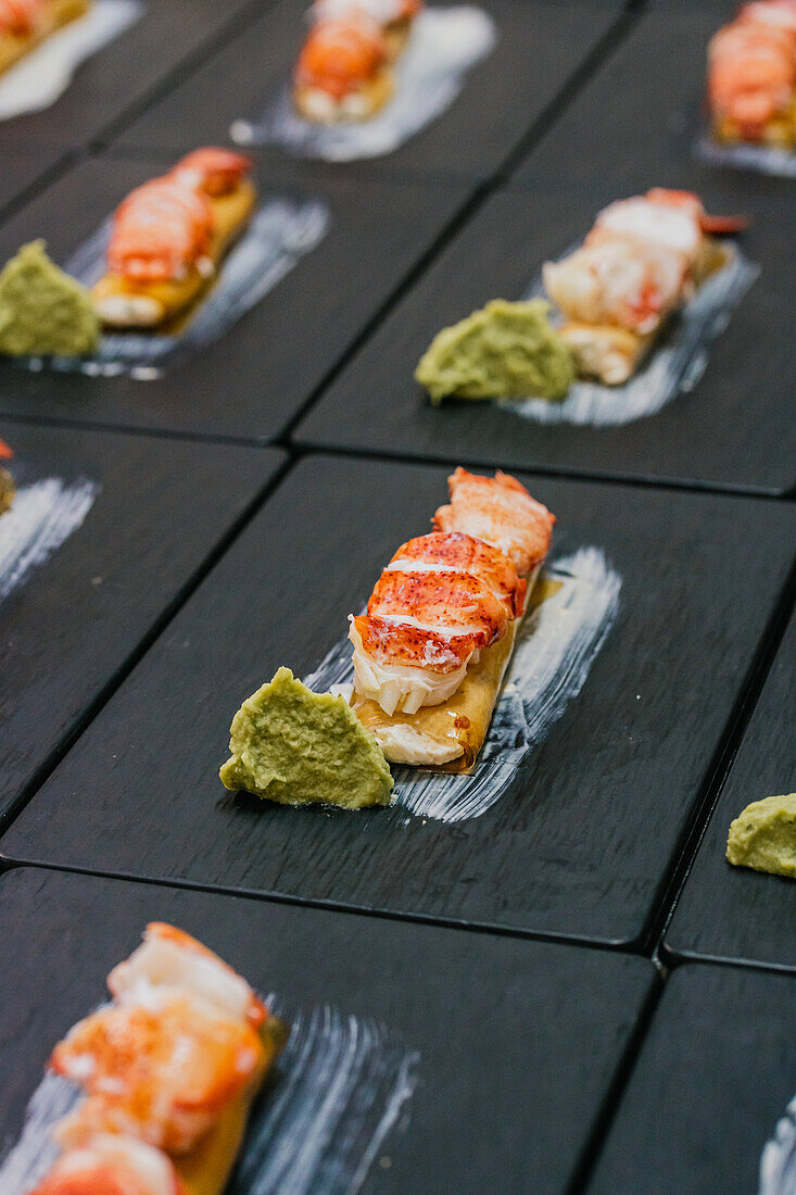 Luxurious lobster canapes paired with a dollop of green sauce, meticulously placed on a chic black slate board for a catered event