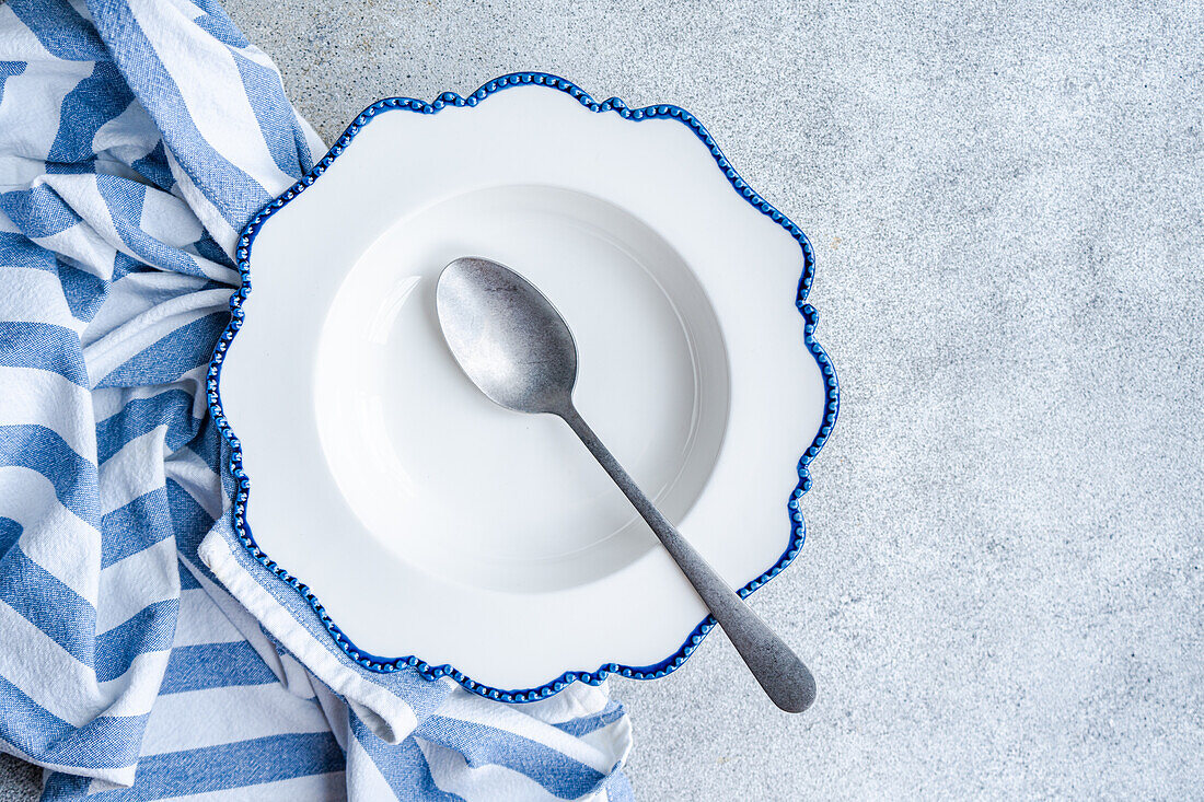 Elegant blue-edged plate with a spoon on a striped cloth over a stone surface, showcasing a clean dining setup